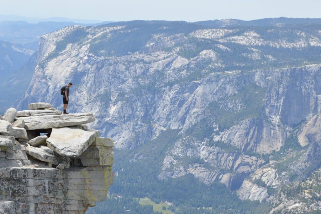 čovjek stoji na stijeni na velikoj visini, a ispred njega su planine
